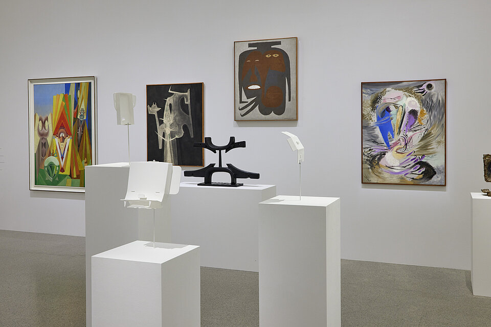 View of an exhibition room with white walls, in the centre an abstract painting of a woman in green and blue dresses by Picasso, on the left and right white bases with small sculptures