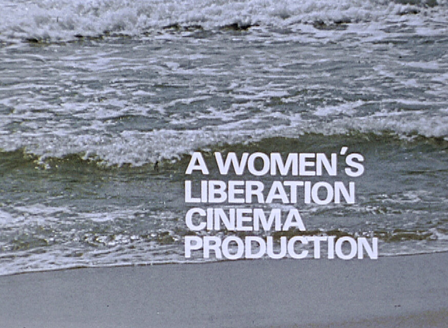 Videostill von an den Strand rollenden Wellen mit dem eingeblendeten weißen Text „A WOMEN’S LIBERATION CINEMA PRODUCTION“. / Film still of waves rolling onto a beach with the white overlaid text “A WOMEN’S LIBERATION CINEMA PRODUCTION”.