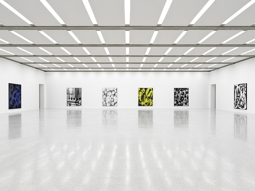 Bright exhibition space with a light-coloured stone floor, abstract works of art in black, white, yellow and blue tones hang on the white walls