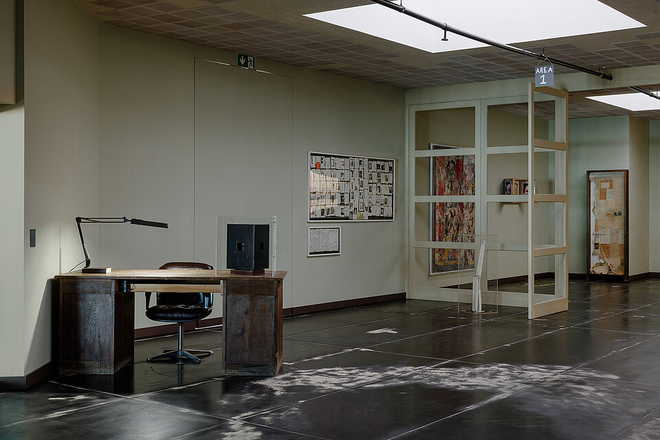 
            
                Ausstellungsbereich mit einem dunklen Schreibtisch, Schreibtischlampe und Drehstuhl
            
        