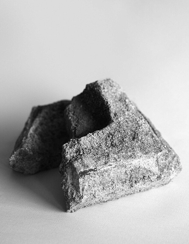 
            
                Schwarz-weiße Nahaufnahme eines rau strukturierten, geometrischen Objekts mit dreieckigen Öffnungen auf hellem Untergrund. / Black-and-white close-up of a rough-textured geometric object with triangular openings placed on a light surface.
            
        