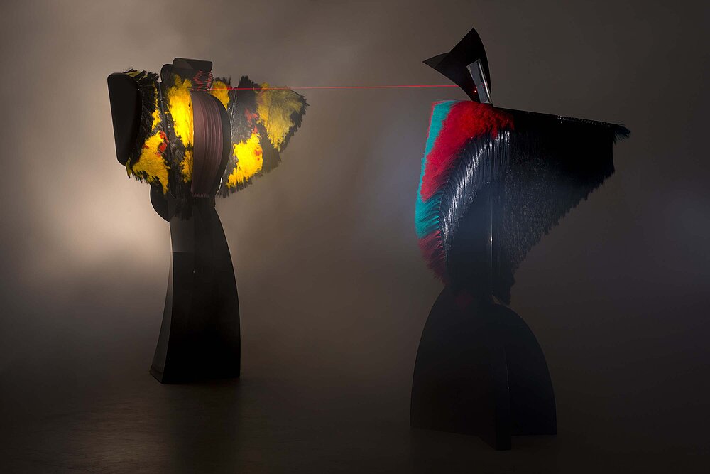 Two mixed media performing sculptures enact a computer controlled 6 minute drama which includes movement, song, the transformation of sound to light, and a laser display