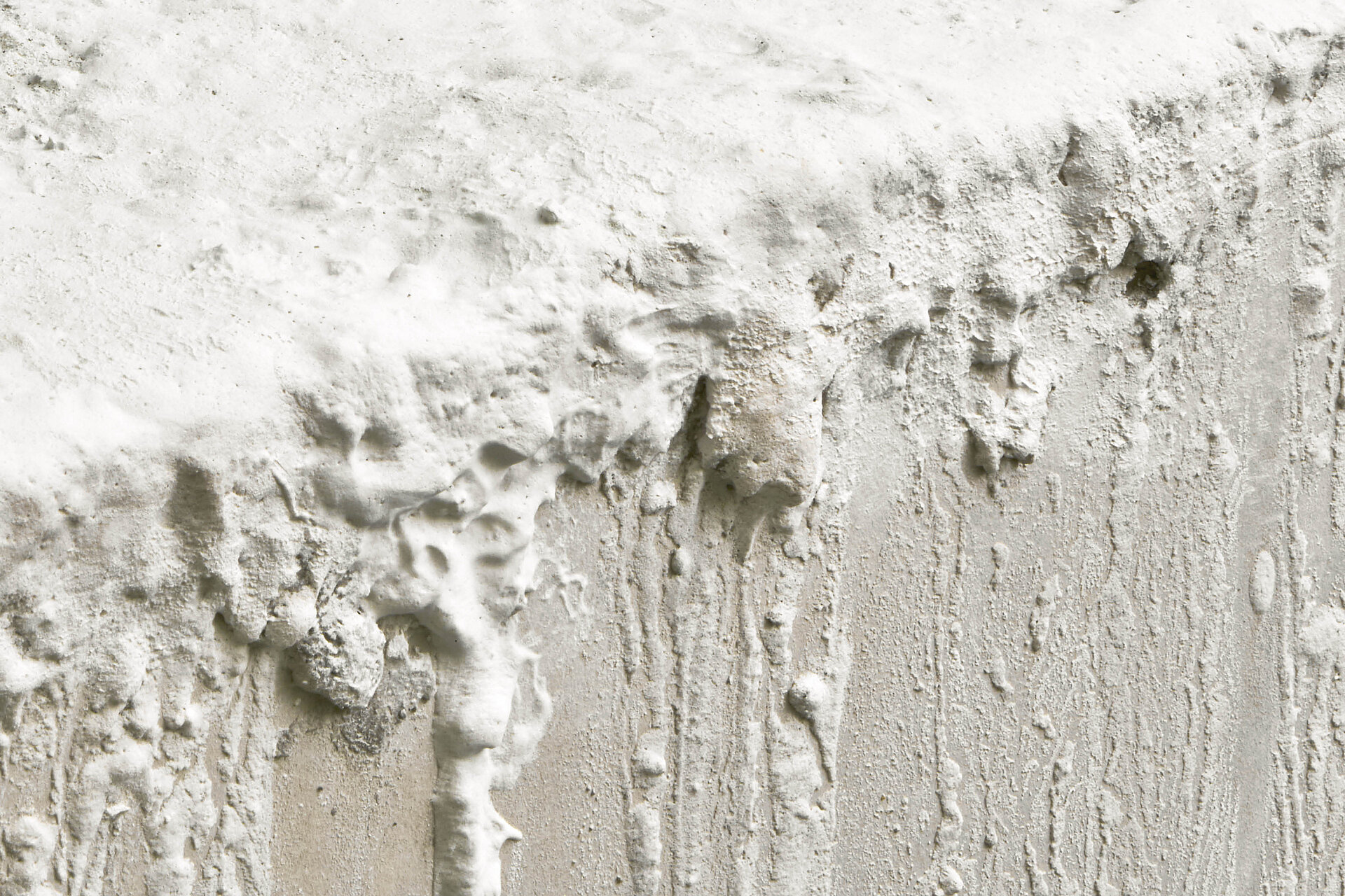 Nahaufnahme einer strukturierten weißen Wandoberfläche mit dicken Farbschichten, Tropfen und unregelmäßigen Erhebungen. / Close-up of a textured white wall surface with thick paint layers, drips, and irregular protrusions.