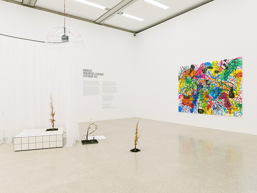 A bright exhibition space, various delicate sculptures at the front left, a large, brightly coloured painting on the wall to the right
