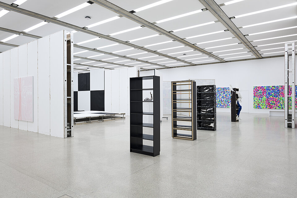  Empty black bookshelves. Behind them, works of art with a chequerboard pattern and pictures in neon colours. 