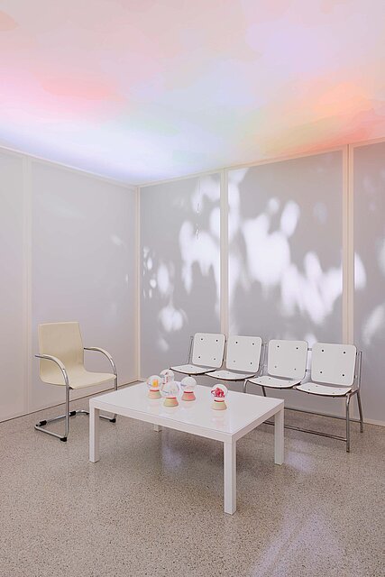 In the centre of the exhibition room is a low white table with snow globes on it. Behind it and to the left of it are a bench and an armchair.