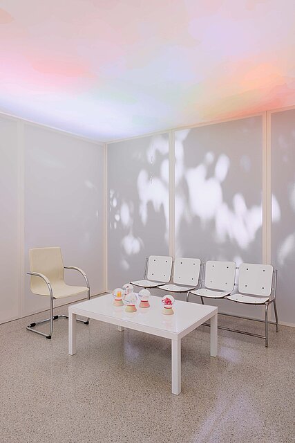 In the centre of the exhibition room is a low white table with snow globes on it. Behind it and to the left of it are a bench and an armchair.