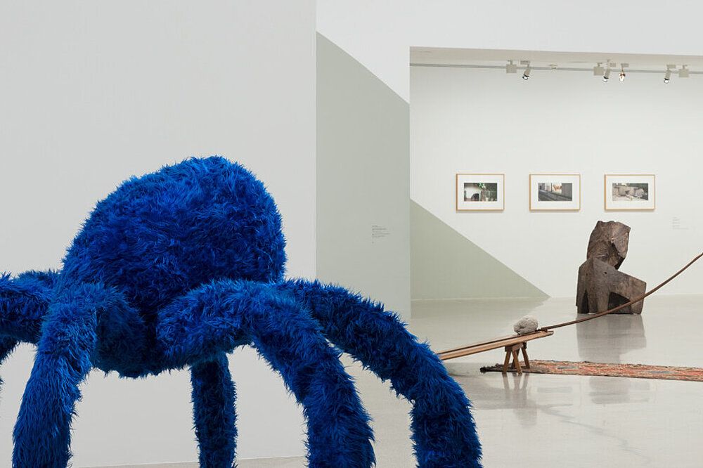 Eine überdimensionierte Spinne mit sechs Beinen aus blauem Kustfell. Dahinter weitere Kunstwerke.