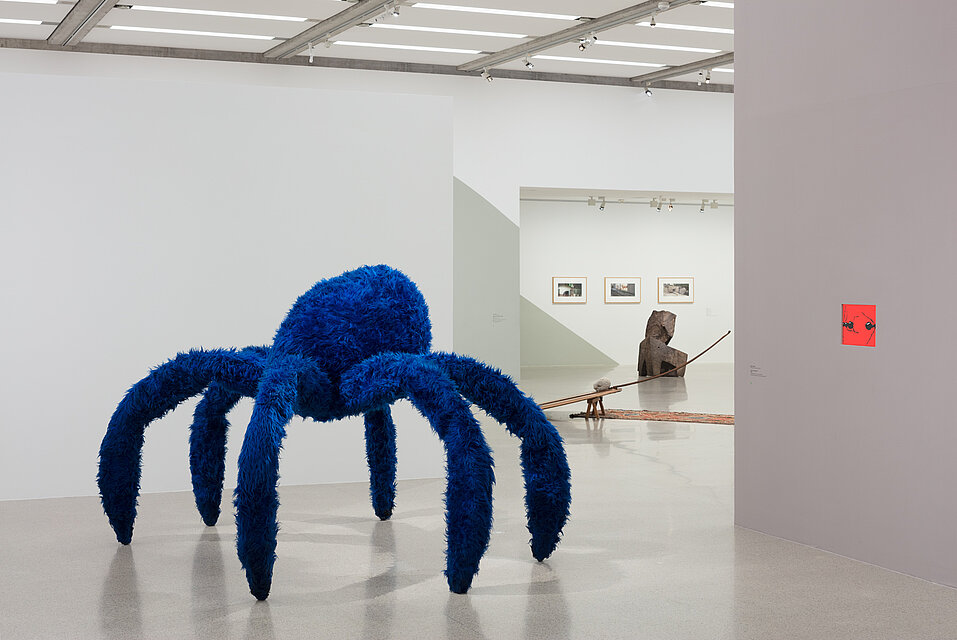 Eine überdimensionierte Spinne mit sechs Beinen aus blauem Kustfell. Dahinter weitere Kunstwerke.