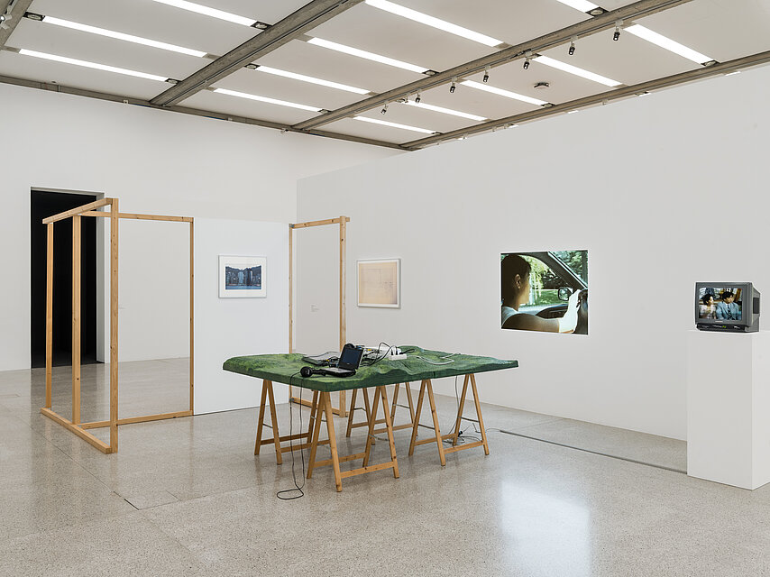 heller Ausstellungsraum, darin verschiedene Kunstwerke, etwa ein Holztisch mit grünem Tuch
