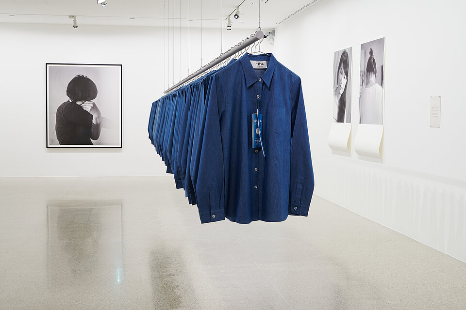  blue shirts on a clothes rail suspended from the ceiling, black and white portrait of a woman in the background on the left
