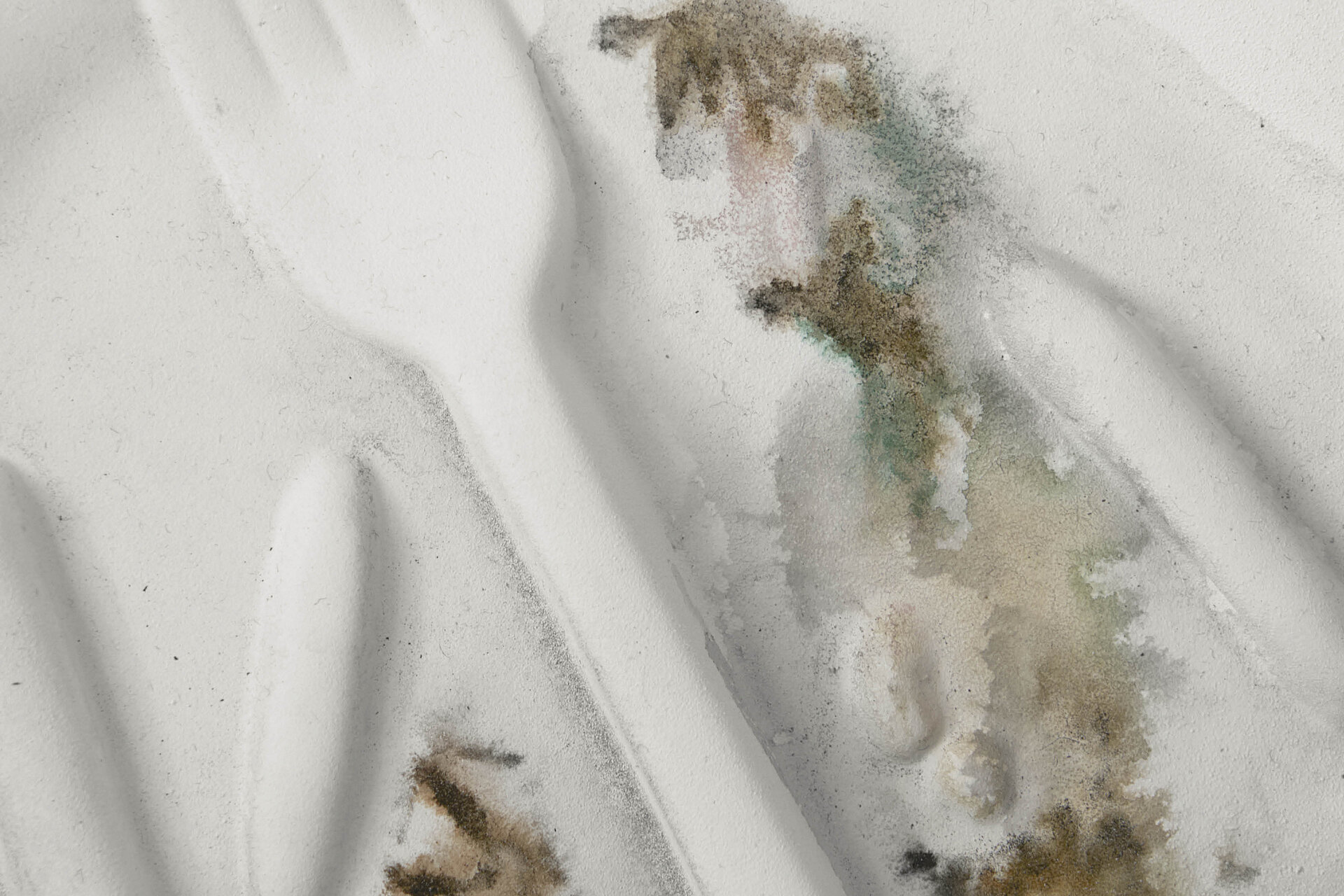 Abstrakte, reliefartige Oberfläche in Weiß mit weichen Faltungen, punktuellen Verfärbungen in Grau‑, Braun‑ und Grüntönen sowie körniger Textur. / Abstract relief-like surface in white with soft folds, localized discolorations in grey, brown, and green tones, and a grainy texture.