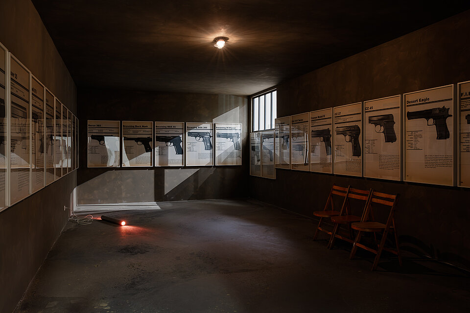 
            
                Dunkler Ausstellungsraum mit gerahmten Tafeln an den Wänden
            
        