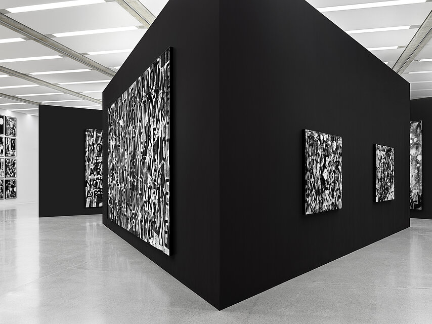 black walls set up in the centre of the exhibition space in the shape of a triangle, with abstract, black and white works of art by Adam Pendleton hanging on the walls