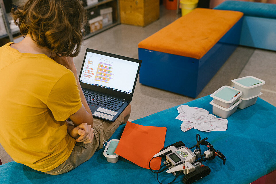 Ein Kind schaut in einen Laptop, daneben ein Roboter