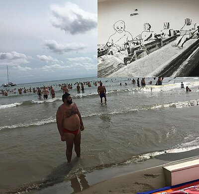 Strandszene mit vielen badenden Personen im flachen Meer unter bewölktem Himmel, überlagert von einer großflächigen Collage, die eine schwarz‑weiße Baustellenlandschaft mit eingezeichneter Figur zeigt. / Beach scene with many people in shallow water under a cloudy sky, overlaid with a large collage depicting a black-and-white construction landscape with a drawn figure.