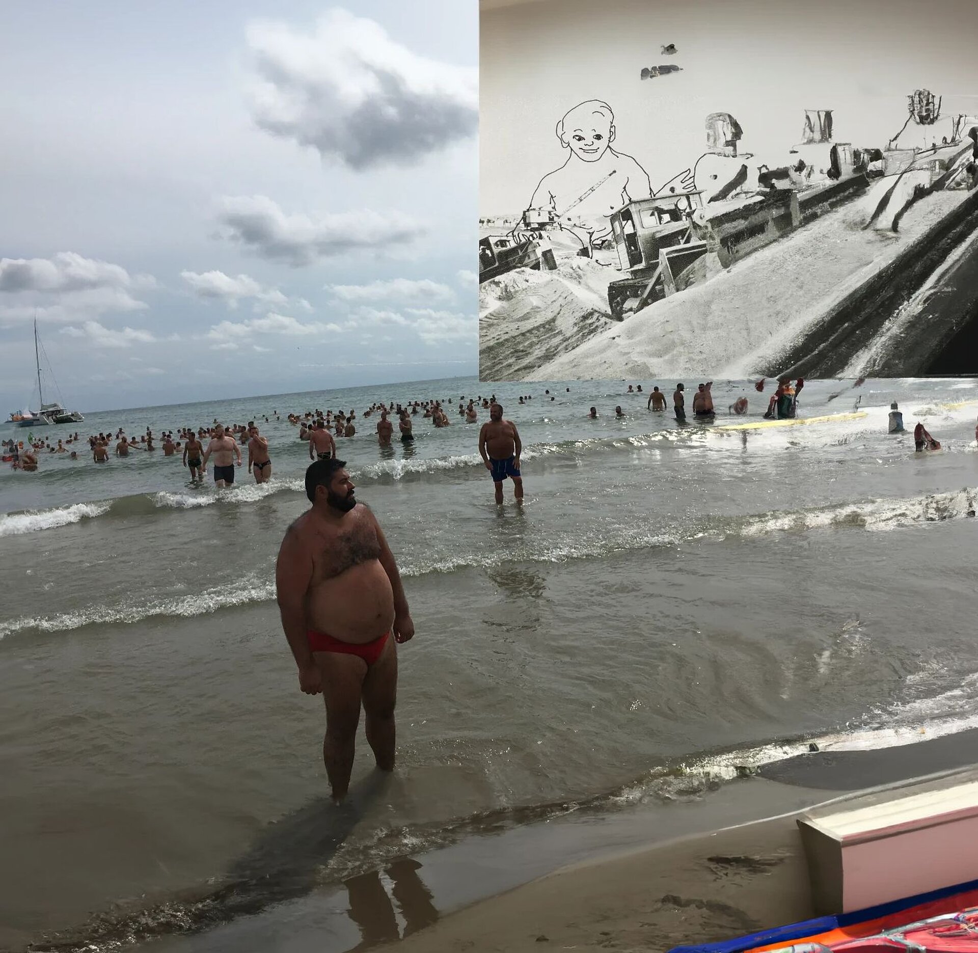 Strandszene mit vielen badenden Personen im flachen Meer unter bewölktem Himmel, überlagert von einer großflächigen Collage, die eine schwarz‑weiße Baustellenlandschaft mit eingezeichneter Figur zeigt. / Beach scene with many people in shallow water under a cloudy sky, overlaid with a large collage depicting a black-and-white construction landscape with a drawn figure.