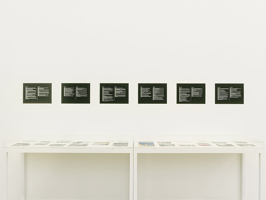 Six black and white pictures hang on a white wall above a white display case