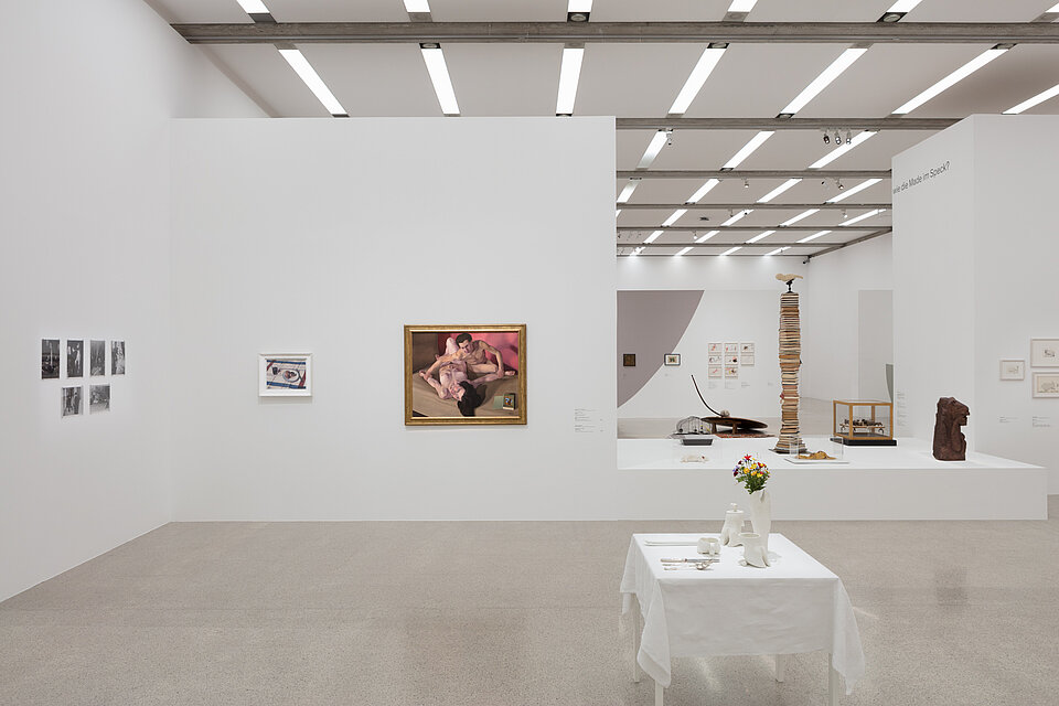 In the centre is a white table with works of art on it. Behind it, works of art on the walls and works of art on a large white base.