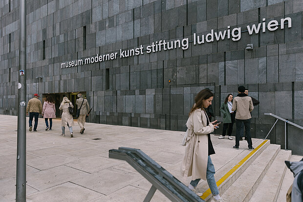 
            
                Menschen vor dem Eingang des mumok, im Vordergrund eine Frau, die die Treppe hinuntergeht, an der Fassade ist der Schriftzug: museum moderner kunst stiftung ludwig wien
            
        