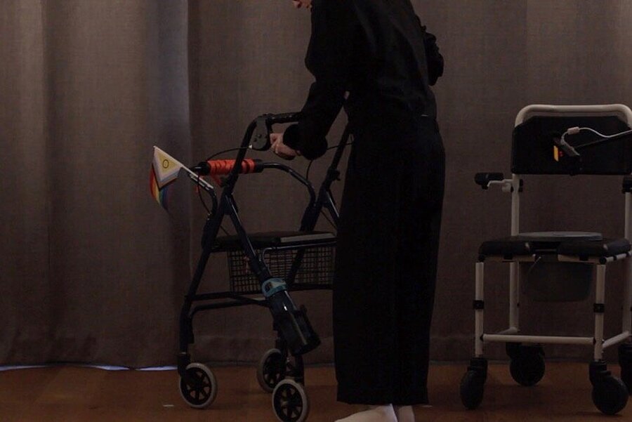 A person is pushing a walker with a Pride flag attached to it.