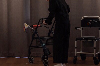 Eine Person schiebt einen Rollator, an dem eine Pride Flagge befestigt ist