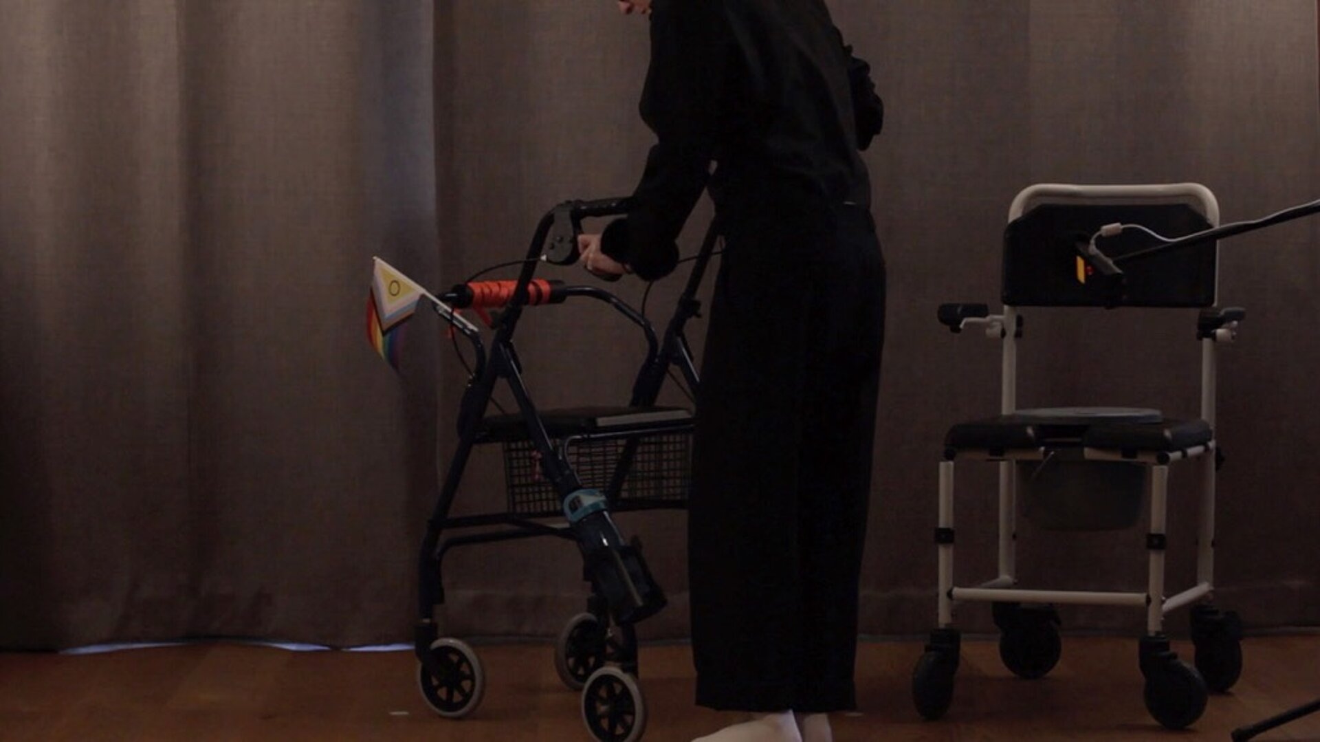 Eine Person schiebt einen Rollator, an dem eine Pride Flagge befestigt ist
