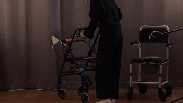 
            
                Eine Person schiebt einen Rollator, an dem eine Pride Flagge befestigt ist
            
        