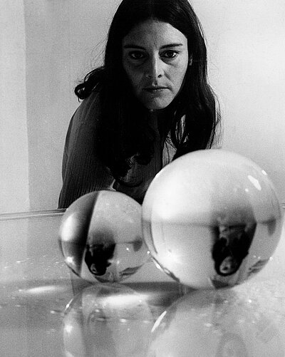 Portrait of Liliane Lijn looking at 2 spheres in front of her.