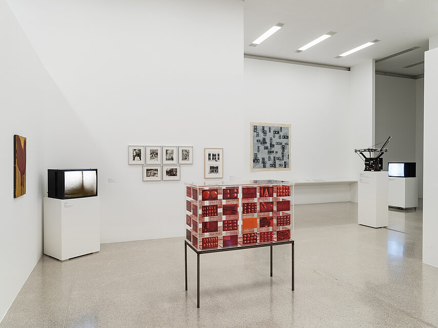 Ausstellungsraum mit mehreren Fernsehern auf Sockeln, in der Mitte ein rotes Kästchen