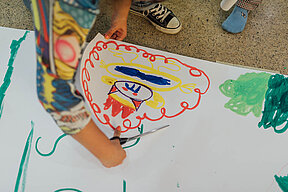 Kinderhand malt ein buntes Bild auf ein großes weißes Papier