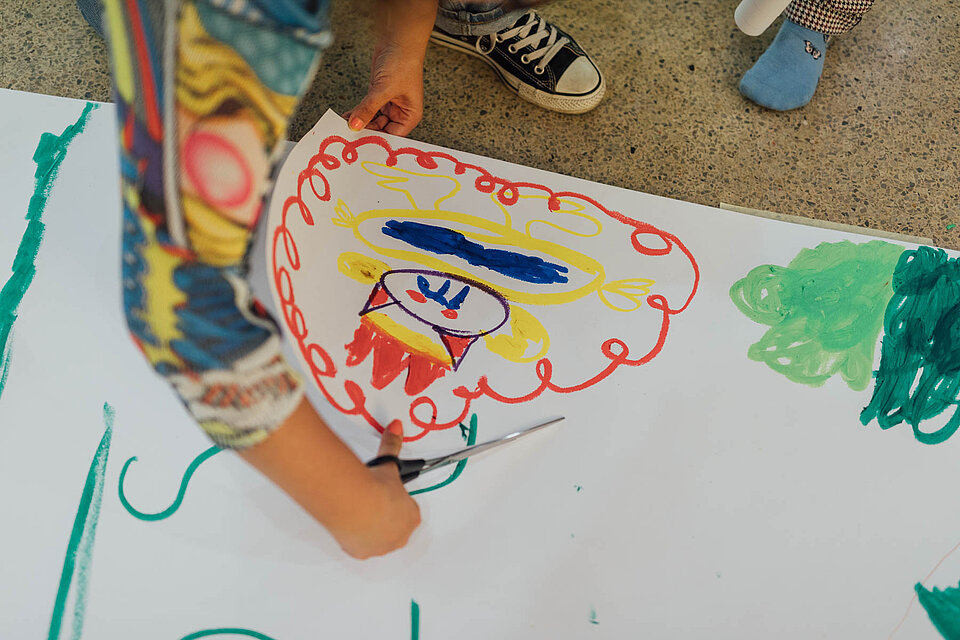
            
                Kinderhand malt ein buntes Bild auf ein großes weißes Papier
            
        