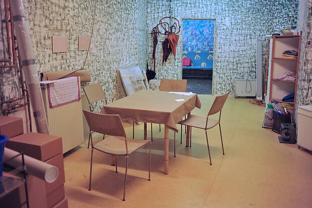 
            
                Blick in einen Raum, in dem ein Tisch mit Stühlen zentral steht, die Wände sind gemustert
            
        