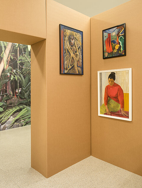 a construction made of cardboard, on the left a kind of passageway with a photo of a jungle, in one corner hang colourful works of art